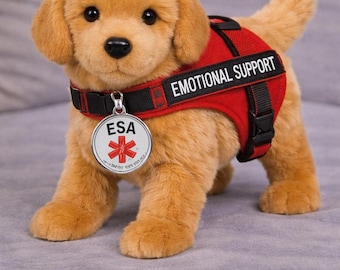 Może przedstawiać: Pluszowy szczeniak golden retriever w czerwonej kamizelce z napisem "EMOTIONAL SUPPORT". Szczeniak ma również obrożę z zawieszką z napisem "ESA" i czerwonym symbolem medycznym.