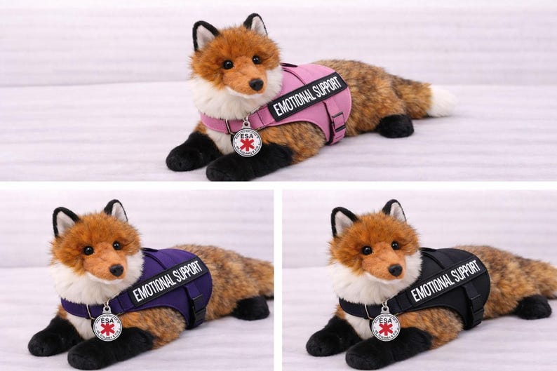 May include: A plush fox toy with brown and white fur, wearing a vest that says "EMOTIONAL SUPPORT." The vest is available in pink, purple, and black. Each fox has a silver ESA tag.