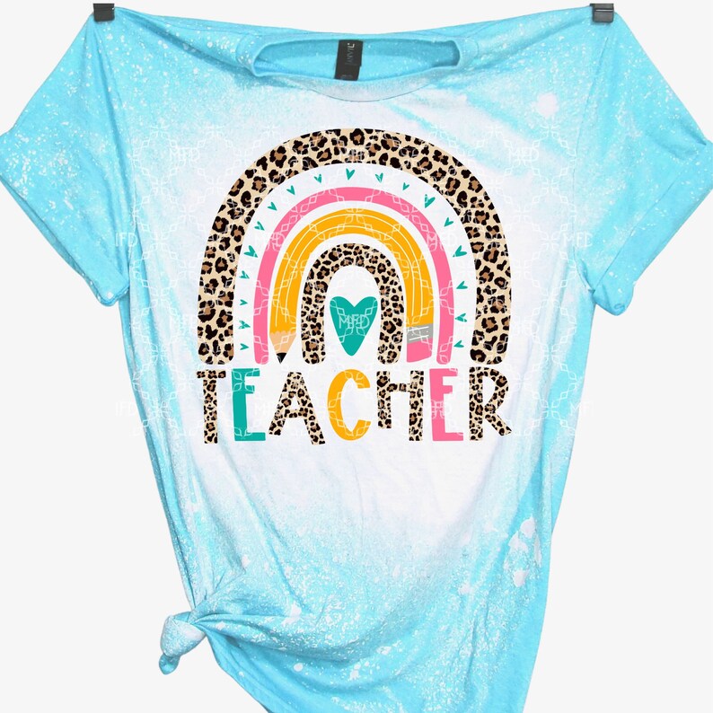 May include: A light blue t-shirt with a bleach-splattered design. The shirt features a rainbow with a leopard print pattern and the word "TEACHER" in colorful letters.