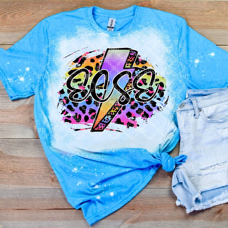 May include: A light blue t-shirt with a bleached design featuring a lightning bolt with the word "Boss" in a rainbow font on a black and pink leopard print background.