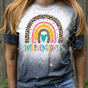 Puede incluir: Una camiseta blanca con un dise&ntilde;o de arco&iacute;ris con estampado de leopardo, l&aacute;pices y un coraz&oacute;n. El texto "Interventionist" est&aacute; impreso debajo del arco&iacute;ris.