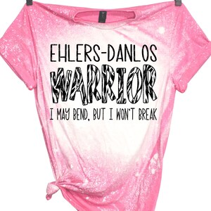 K&ouml;nnte beinhalten: Rosa gebleichtes T-Shirt mit einem schwarz-wei&szlig;en Zebra-Muster, auf dem "Ehlers-Danlos Warrior I may bend, but I won't break" steht.