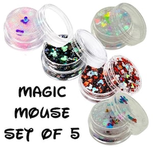 May include: A set of five small clear plastic jars filled with colorful decorative glitter in various shapes, including mouse head silhouettes. The text MAGIC MOUSE SET OF 5 is printed in black on the left side of the image against a white background.