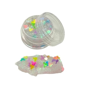 May include: Clear plastic jar filled with iridescent glitter and colorful Mickey Mouse-shaped confetti. A small pile of glitter and confetti sits below the jar. The confetti includes pink, yellow, green, and purple colors.