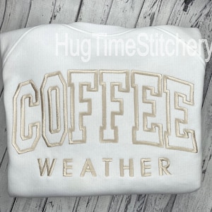 May include: White sweatshirt with the words "COFFEE WEATHER" embroidered in a light brown color.