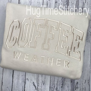 May include: A beige sweatshirt with the text "COFFEE WEATHER" embroidered in a light brown color.