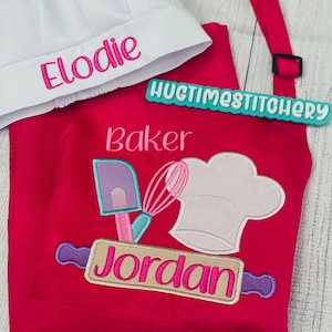 May include: A bright pink apron and a white chef hat. The hat features the embroidered name Elodie in pink. The apron displays the text Baker, a purple spatula, a pink whisk, a white chef hat, and the name Jordan in pink on a rolling pin.
