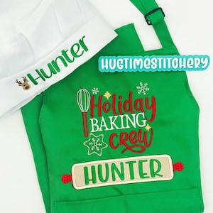May include: A green apron and chef's hat set. The apron features the text "Holiday Baking Crew" and "Hunter" embroidered in red and green. A whisk and snowflakes are also embroidered on the apron. The chef's hat is white with the name "Hunter" embroidered in green.