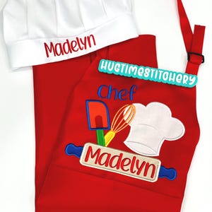 May include: A red apron and white chef hat set featuring embroidered kitchen tools, a rolling pin, and the name Madelyn in red and blue thread. The apron includes the text Chef and HUGTIMESTITCHERY, while the hat displays the name Madelyn.