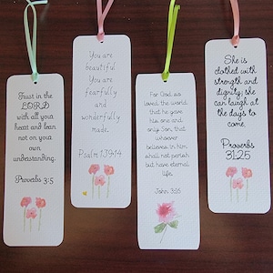 May include: Four white bookmarks with inspirational quotes and floral watercolor designs. Each bookmark has a different ribbon color. The text includes Bible verses from Proverbs and John.