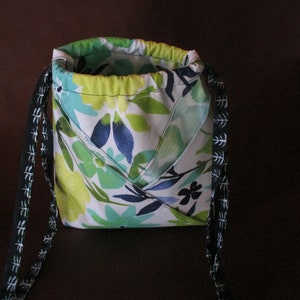 May include: A small drawstring bag with black and white patterned straps. The bag is made of white fabric with a floral pattern in shades of green, blue, and white.