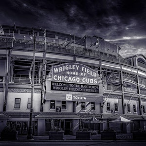 May include: A black and white photo of Wrigley Field, home of the Chicago Cubs. The sign above the entrance reads "Wrigley Field, Home of Chicago Cubs". A banner below the sign reads "Welcome to the Hartford's Wrigley Field Experience!" with the Toyota logo below the banner.