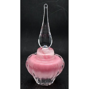 May include: A clear glass perfume bottle with a pink interior and a clear, elongated stopper. The bottle has a rounded base and a decorative, ridged design. The stopper is long and slender, with a rounded top.