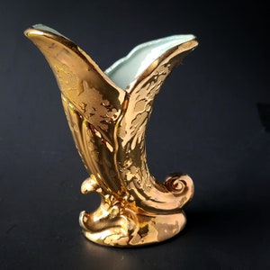May include: A gold ceramic vase in the shape of a horn with a light blue interior. The vase is decorated with a floral pattern.