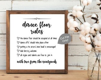 May include: A framed sign with the text "dance floor rules" in black script. The sign includes a list of rules and is decorated with hearts. A vase of cotton stems sits to the right of the sign.