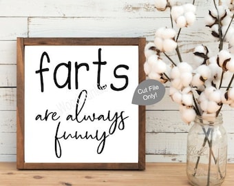 Può includere: Un cartello in legno incorniciato con la scritta nera "farts are always funny". Un vaso di steli di cotone è a destra del cartello. Il cartello è su una superficie di legno.