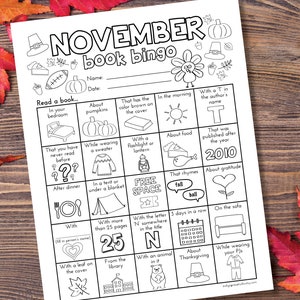 May include: A printable November book bingo card with a turkey and fall-themed illustrations. The card has squares with prompts like "Read a book in your bedroom", "About pumpkins", "That has the color brown on the cover", "With a T in the author's name", "That was published after the year 2010", "About gratitude", "With the letter N somewhere in the title", "3 days in a row", "On the sofa", "About Thanksgiving", and "While wearing your PJs".