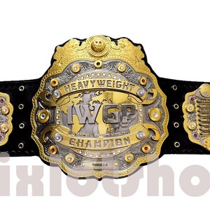 Könnte beinhalten: Ein gold- und silberner Meisterschaftsgürtel mit einer großen Mittelplatte, auf der "IWGP Heavyweight Champion" steht. Der Gürtel hat ein schwarzes Lederband mit mehreren kleineren Platten, auf denen die Namen vergangener Champions stehen.