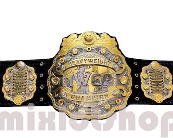 May include: A gold and silver championship belt with a large central plate that reads "IWGP Heavyweight Champion". The belt has a black leather strap with multiple smaller plates featuring names of past champions.