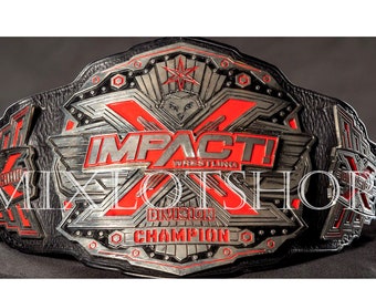 May include: A silver and black wrestling championship belt with red accents. The belt features the words "Impact Wrestling" and "Division Champion".