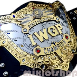 Könnte beinhalten: Ein goldener und silberner Meisterschaftsgürtel mit der Aufschrift "IWGP World Heavyweight Champion". Der Gürtel hat ein schwarzes Lederband und eine große, verzierte Mittelplatte.