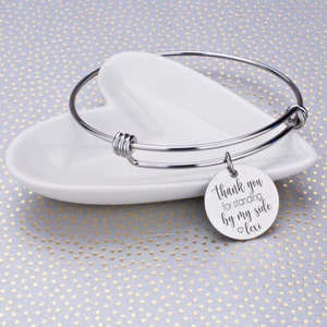 May include: Silver expandable bangle bracelet with a round charm that reads "Thank you for standing by my side Lexi".