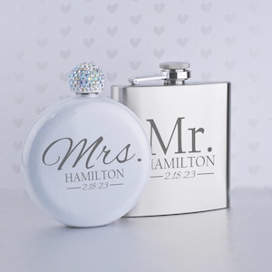 Puede incluir: Dos matraces de cadera plateados con un tapón adornado con cristales. El matraz de la izquierda es blanco y dice "Mrs. HAMILTON - 2.18.23". El matraz de la derecha es plateado y dice "Mr. HAMILTON - 2.18.23".