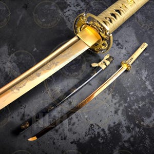Könnte beinhalten: Ein goldenes Katana und eine kleinere Tanto-Klinge werden gezeigt. Das Katana hat eine goldfarbene Klinge mit einer Drachengravur, einen goldenen Griff und eine schwarz-goldene Scheide. Das Tanto hat eine goldene Klinge und einen goldenen Griff.