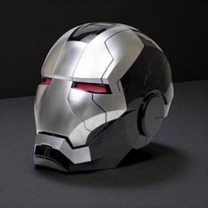 Puede incluir: Un casco plateado y negro con ranuras rojas para los ojos. El casco tiene un acabado metálico y un diseño angular, que se asemeja a una máscara de superhéroe. El casco es una réplica del casco de un personaje de una película popular.