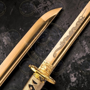 Puede incluir: Una katana dorada con un grabado de dragón en la hoja. La empuñadura y la guarda también son doradas, con diseños intrincados. La vaina es de color marrón claro. La espada se exhibe sobre una superficie oscura.