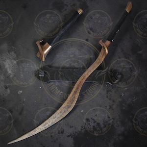 May include: A curved, bronze-colored sword with a black handle and a matching scabbard. The blade has a worn, textured appearance. The hilt features a distinctive, angular design. The sword is displayed on a dark surface.