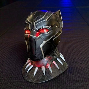May include: Black Panther helmet replica with glowing red eyes and silver accents. The base features white claw-like details and a textured surface. A detailed collectible inspired by the Marvel superhero.