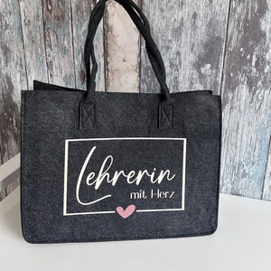 May include: A gray felt tote bag with white text that says "Lehrerin mit Herz" and a pink heart.