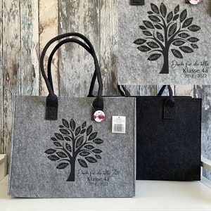 Könnte beinhalten: Zwei graue und schwarze Filztaschen mit schwarzen Baummotiven und Namen auf den Blättern. Der Text auf der Tasche lautet "Danke für die tolle Zeit Klasse 4a 2018-2022".