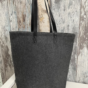 May include: A gray felt tote bag with black leather handles. The bag has a simple design and is perfect for carrying everyday essentials.