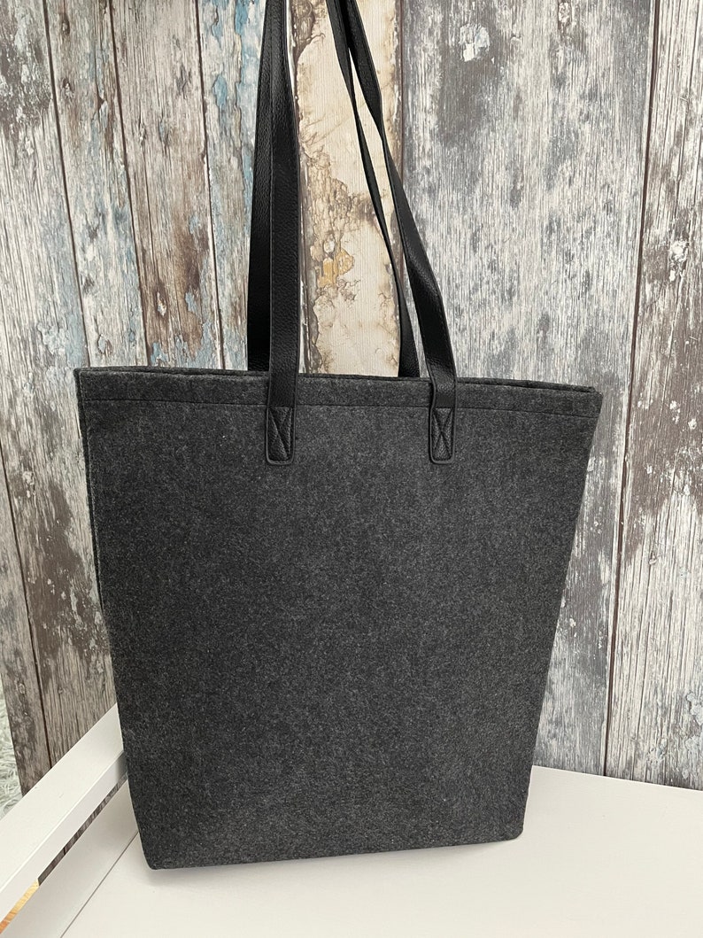 May include: A gray felt tote bag with black leather handles. The bag has a simple design and is perfect for carrying everyday essentials.