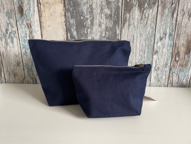May include: Two navy blue zippered pouches, one larger than the other, on a white surface.
