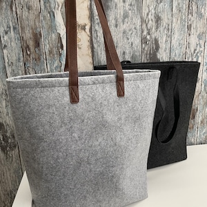 May include: Two felt tote bags, one gray with brown leather handles and one black with black handles.