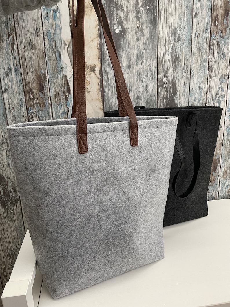 May include: Two felt tote bags, one gray with brown leather handles and one black with black handles.