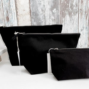 May include: Three black canvas zippered pouches of different sizes. The pouches are lined up from largest to smallest.