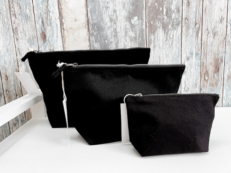 May include: Three black canvas zippered pouches of different sizes. The pouches are lined up from largest to smallest.
