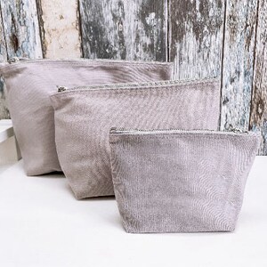 May include: Three gray zippered pouches of different sizes. The pouches are made of a soft, textured fabric.