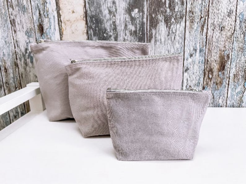 May include: Three gray zippered pouches of different sizes. The pouches are made of a soft, textured fabric.