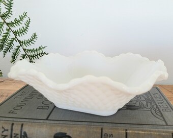 May include: A white milk glass bowl with a scalloped edge and a textured design. The bowl is sitting on a book.