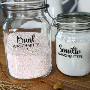 Può includere: Due barattoli di vetro trasparente con chiusure in metallo, riempiti di detersivo per bucato. Un barattolo ha granuli rosa e bianchi e il testo "Bunt Waschmittel". L'altro barattolo ha granuli bianchi e il testo "Sensitiv Waschmittel".