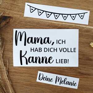 May include: White sticker with the text "Mama, ICH HAB DICH VOLLE Kanne LIEB!" in black script. A smaller sticker reads "Deine Melanie". A banner with heart-shaped flags is also included. The stickers are on a wooden surface.