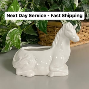 May include: White ceramic planter shaped like a laying down unicorn. The planter has a small opening on the back for drainage.