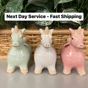 May include: Three ceramic unicorn planters in green, white, and pink. The planters are sitting on a wicker basket.