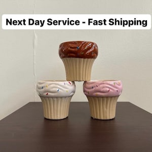 May include: Three ceramic cupcake-shaped planters, one brown with chocolate sprinkles, one white with colorful sprinkles, and one pink with colorful sprinkles.