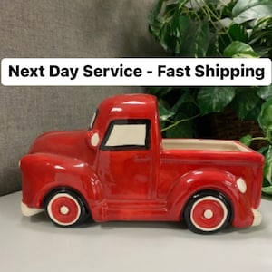 May include: A ceramic red pickup truck planter with white accents on the wheels and trim. The truck has a rectangular bed for planting. The text "Next Day Service - Fast Shipping" is at the top.